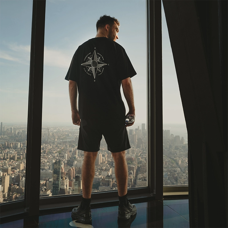 Oliver Heldens from behind in a black compass t-shirt, at a high window over a city