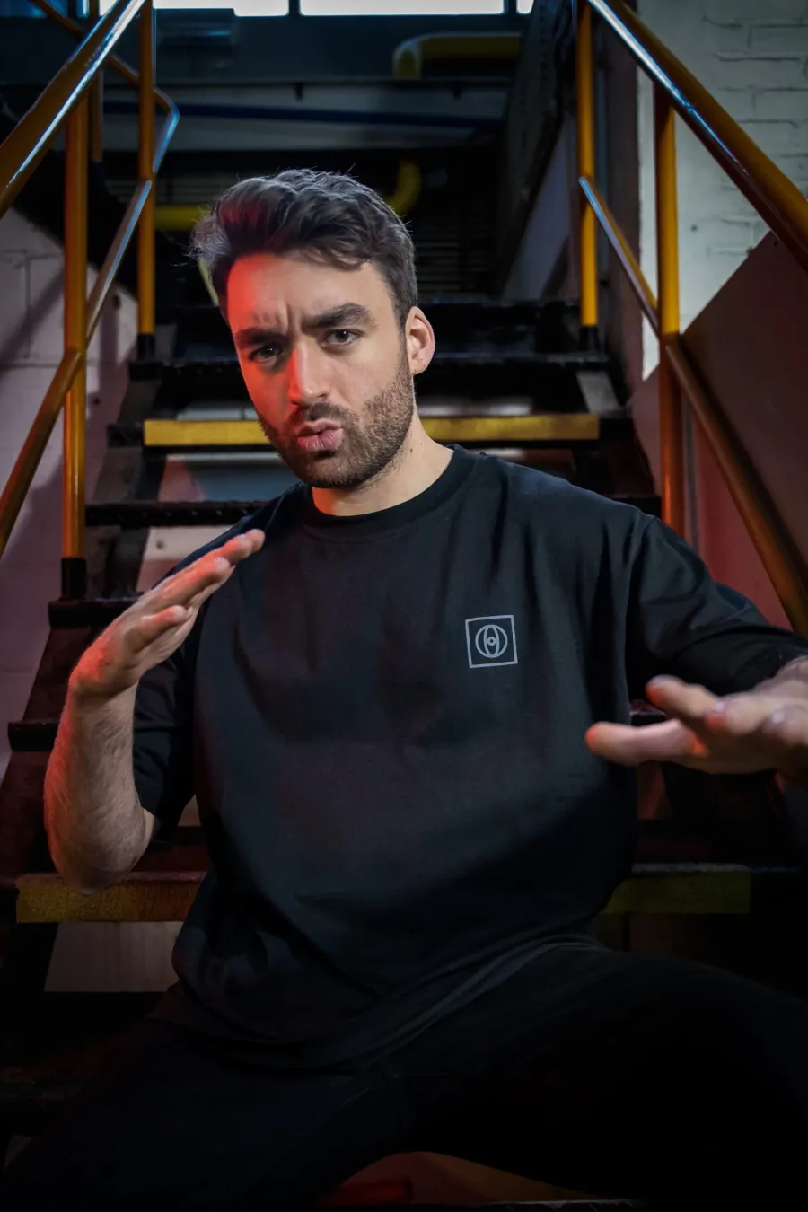 Oliver Heldens seated on stairs in a black t-shirt with a small chest logo
